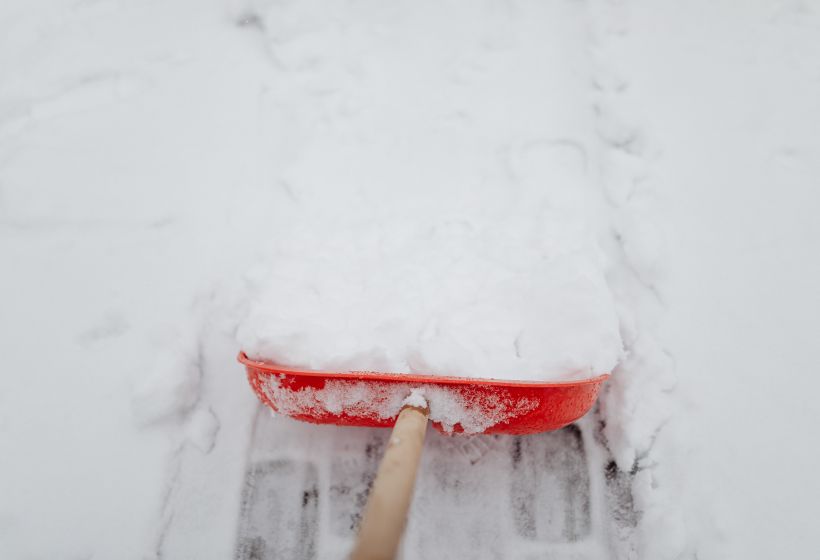 Clearing snow from a driveway with a red shovel